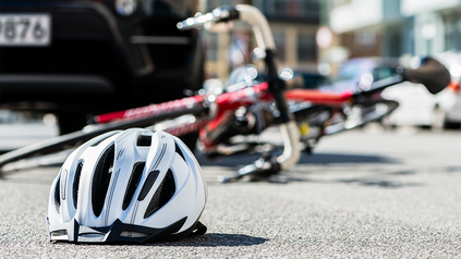 Fahrradhelm, dahinter Fahrrad, dass am Boden liegt, weil es von einem Auto angefahren wurde.