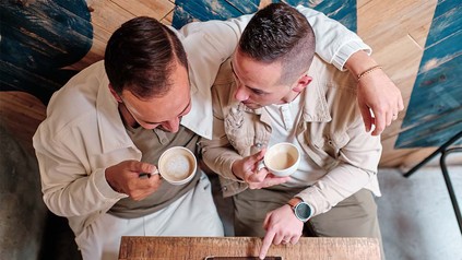 Zwei Männer nebeneinander mit Kaffee in einem Café.