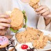 Viel Essen wie Burger und Donuts vor einer jungen Frau auf dem Tisch.