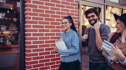 Drei lächelnde Studierende, die über den Campus laufen.