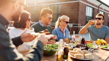 Junge Leute an Tisch mit Bier und Gegrilltem.