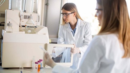 Zwei junge Frauen mit Laborkitteln und Sicherheitsbrillen im Labor.