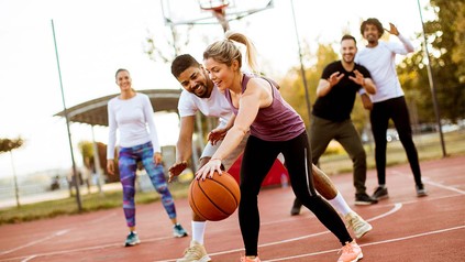 Gruppe Studierender, die auf dem Sportplatz Basketball spielen.