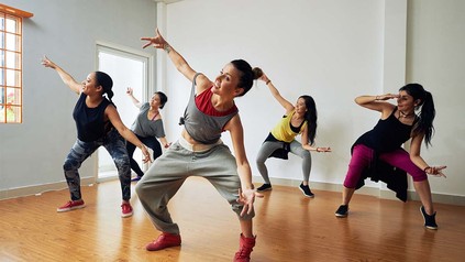 Fünf Frauen in Sportklamotten im Tanzstudio, die zusammen HipHop tanzen.