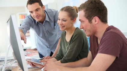 Drei Studierende zusammen vor Bildschirmen.