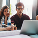 Gruppe diverser Studierender gemeinsam vor Laptop an Schreibtisch.