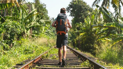 Junger Mann mit Rucksack unterwegs in den Tropen. (Foto: © NDStock/GettyImages)