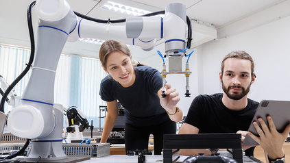 Werkstudentin und Werkstudent vor Roboterarm in Labor.