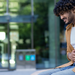 Junger Mann auf Bank vor Fakultät, der sich mit schmerzverzerrtem Gesicht den Bauch hält.