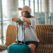 Junge Frau am Flughafen auf einer Bank am Terminal sitzend mit Koffer.