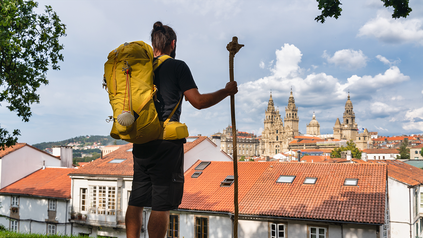 Junger Mann mit Backpack und Wanderstock vor Santiago de Compostela.