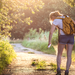 Junge Frau mit kurzen Hosen beim Spaziergang im Wald; um sie rum Mücken, sie sprüht sich Mückenspray auf die Beine.