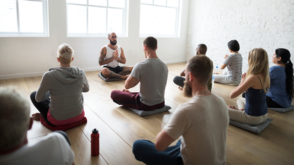 Gruppenmeditation ins Studio. Alle sitzen im Schneidersitz auf Yogamatten.