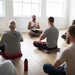 Gruppenmeditation ins Studio. Alle sitzen im Schneidersitz auf Yogamatten.