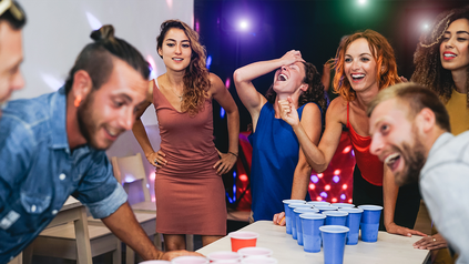 Junge Leute, daheim, um einen Tisch, auf dem sie Bierpong spielen.