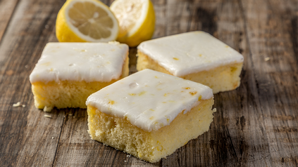 Drei viereckige Zitronenkuchenstücke mit Glasur auf Holzbrett.