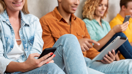 Vier junge Menschen sitzen und haben alle ihr Smartphone in den Händen.