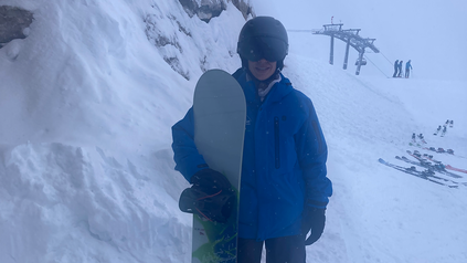 Stefanie Hafeneder in Skimontur am Berg mit ihrem Snowboard in der Hand.