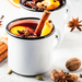 Glühwein in weißer Emaile-Tasse mit Orangenschalen und Zimtstangen drapiert.