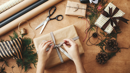 Tisch, auf dem Geschenke, Geschenkpapier, Schere und andere Verpackungsmaterialen liegen.