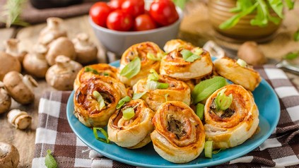 Pizzaschnecken zusammen mit Pilzen und Tomaten auf einem blauen Teller.