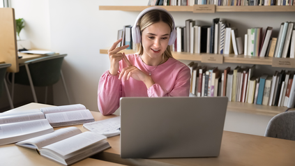 Studentin an einem Arbeitsplatz in der Bibliothek. Sie trägt Kopfhörer und vor ihr ist ein Laptop aufgeklappt.