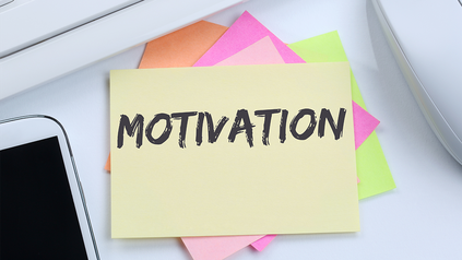 Ausschnitt von Arbeitsplatz mit Handy, Computermaus und Notizzettelblock, auf dem oben 'Motivation' steht.