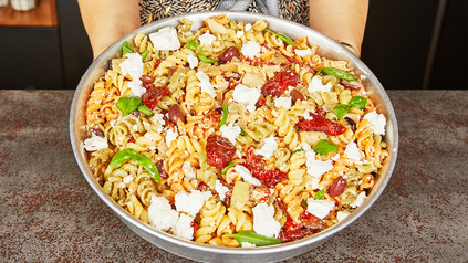 Große Schale mit Nudelsalat mit Käse, getrockneten Tomaten, Oliven und Rucola.
