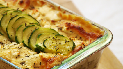 Ausschnitt von fertiger Zucchini-Lasagne in Glasform auf Holzbrett.