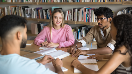 Vier junge Studierende an einem Schreibtisch in der Bibliothek.