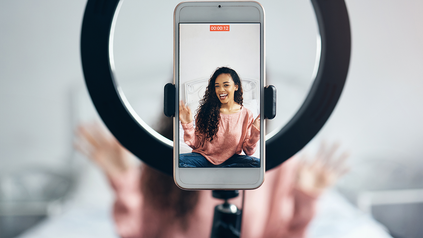 Junge Frau, die sich gerade mit ihrem Smartphone und Selfie-Ringlicht filmt.