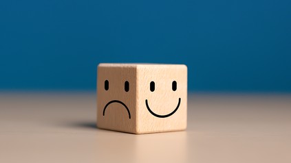 Holzwürfel auf dem Tisch, eine Seite zeigt einen lachenden Smiley, die andere Seite einen traurigen Smiley